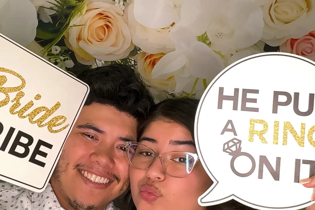 Happy couple at engagement photo booth with "Bride Tribe" and "He Put a Ring on It" signs